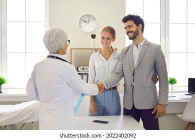 Happy Patients Shaking Hands With Doctor. Young Married Couple Planning To Have Baby And Seeing Family Practitioner For Health Exam. Future Parents Exchange Handshake With OB GYN Pregnancy Specialist