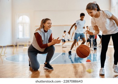 Happy PE teacher encouraging her student during basketball practice at school gym. 