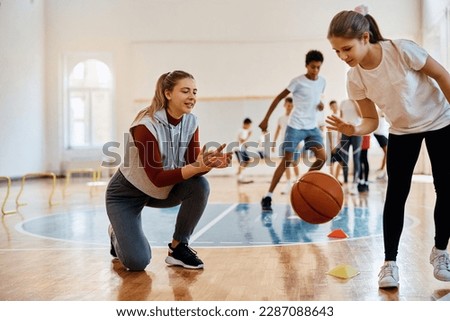 Happy PE teacher encouraging her student during basketball practice at school gym. 
