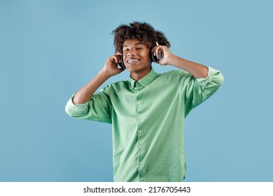 Happy peaceful african american guy listening to music in wireless headset, closing eyes and relaxing, standing over blue background. Positive teenager enjoying favorite playlist - Powered by Shutterstock