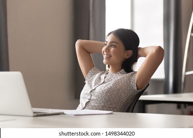 Happy Peaceful Asian Female Employee Lean On Comfortable Office Chair, Holding Hands Behind Head, Relaxing During Working Day Break Or After Completed Job, Looking Aside, Dreaming About Vacation.