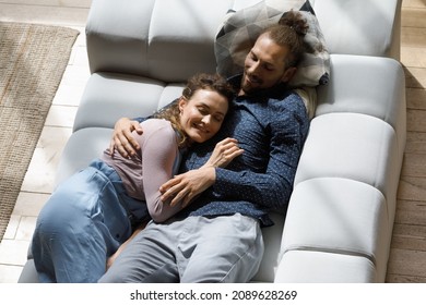 Happy peaceful couple resting on soft couch, lying together. Sweet dating girl and guy relaxing on comfortable couch in living room, enjoying leisure, lazy weekend break at home. Top view