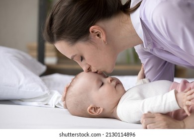 Happy peaceful mew mom kissing cute baby lying on bed, calming infant kid for sleeping, cuddling child with love, tenderness, affection, devotion. Motherhood, parenthood concept