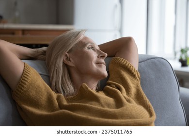 Happy peaceful middle aged lady relaxing on home sofa, looking at window away, enjoying relaxation, leisure, break, thinking, dreaming, smiling at good thoughts, taking deep breath of fresh air - Powered by Shutterstock