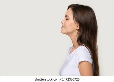 Happy peaceful millennial girl stand in profile side view isolated on grey studio background, calm young woman in white t-shirt with eyes closed face blank copy space, massage or healthcare sale offer