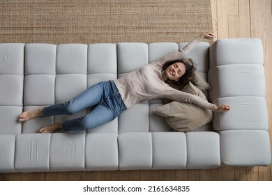 Happy peaceful young woman relaxing on comfortable couch at home with closed eyes, stretching hands and body, smiling, laughing, enjoying relaxation, leisure, weekend, lying on back. Full length - Powered by Shutterstock