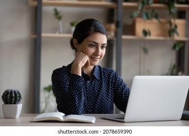 Happy Pensive Young Indian Ethnicity Businesswoman Looking At Computer Screen, Working On Online Project On Computer At Home Or Office, Analyzing Electronic Document, Using Software Applications.