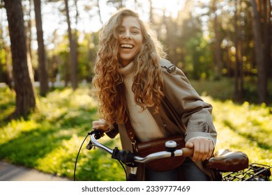Happy pensive young woman in stylish clothes riding a bike in a sunny park, outdoors, looking away. Active lifestyle. The concept of nature. - Powered by Shutterstock