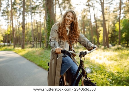 Happy pensive young woman in stylish clothes riding a bike in a sunny park, outdoors, looking away. Active lifestyle. The concept of nature.