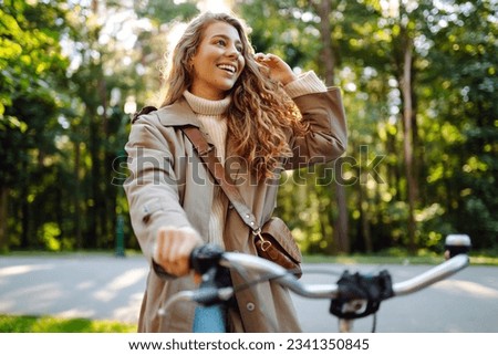Happy pensive young woman in stylish clothes riding a bike in a sunny park, outdoors, looking away. Active lifestyle. The concept of nature.