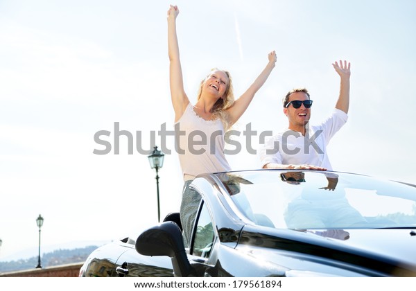 Happy people in car driving on road trip. Young\
couple having fun dancing and cheering in car driving on travel\
vacation together. Lifestyle with beautiful cheerful lovers, young\
woman and man.