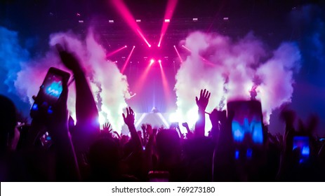 Happy people dance in nightclub party concert and listen to the music from DJ on the stage in the background.