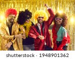 Happy people dancing gangnam style on stage with shiny golden background. Group of friends disguised in boas, glasses, sequin jackets and funny silly curly wigs having fun at night club disco party