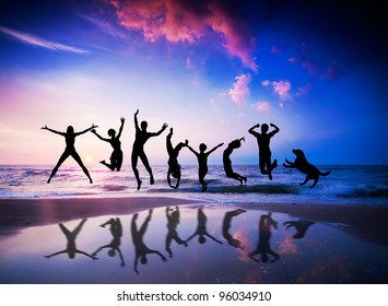 Happy People And Dog Jumping Together On The Sunset Beach