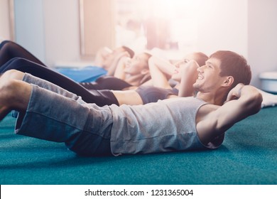 Happy people doing an exercise on a crunches lying. Young men and women perform a physical exercise on the press in the supine position to improve the shape. Group fitness training of people