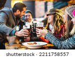 Happy people drinking beer at brewery bar out side - Beverage life style concept with guys and girls enjoying winter time together at open air restaurant patio - Warm filter with focus on glasses