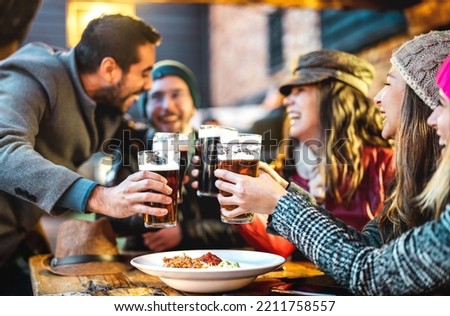 Happy people drinking beer at brewery bar out side - Beverage life style concept with guys and girls enjoying winter time together at open air restaurant patio - Warm filter with focus on glasses