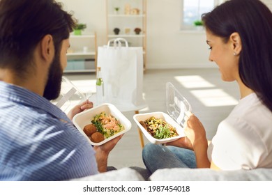 Happy People Enjoying Takeout Lunch At Home. Young Couple Sitting On Sofa And Eating Fresh Healthy Takeaway Food From Plastic Containers. Man And Woman Comparing Two Meals Ordered In Delivery Service