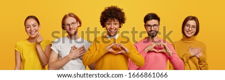 Happy people express love and gratitude, shape hearts to camera, confess in good feelings, woman and man touched by heartwarming words. Group of diverse men and women pose over yellow studio wall