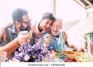 Happy People Family Concept Laugh And Have Fun Together With Three Different Generations Ages : Grandfather Father And Young Teenager Son All Together Eating At Lunch - Outdoor Home Party Leisure