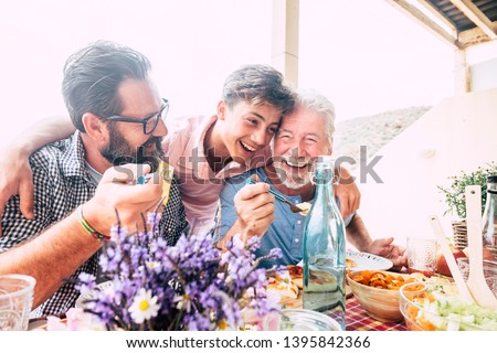Happy people family concept laugh and have fun together with three different generations ages : grandfather father and young teenager son all together eating at lunch - outdoor home party leisure