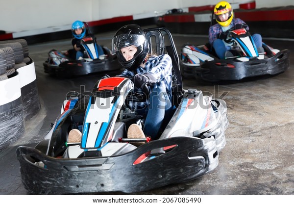 Happy people in helmets driving cars for karting\
in sport club indoor
