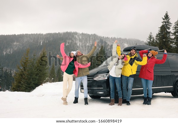 Happy people jumping near car on snowy road.\
Winter vacation