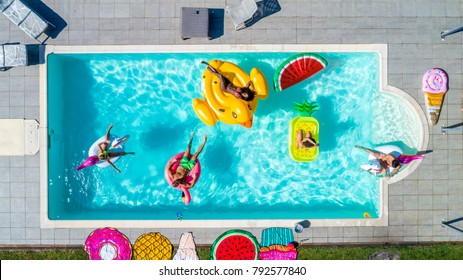 Happy people partying in an exclusive swimming pool with animal and fruit shapes mats, view from above - Powered by Shutterstock