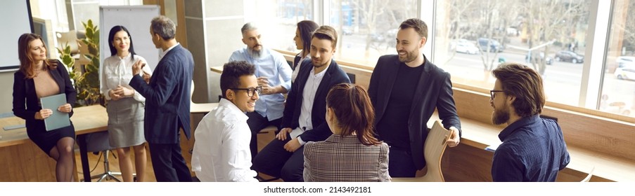 Happy People Standing In Modern Office And Talking. Multiracial Group Of Men And Women Discussing Team Training Workshop They Have Just Attended. Employees Having Break During Business Seminar