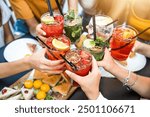 Happy people toasting cocktail glasses sitting at bar table - Cheerful friends enjoying happy hour at pub restaurant balcony - Food and beverage life style concept