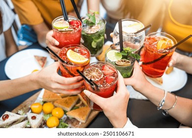 Happy people toasting cocktail glasses sitting at bar table - Cheerful friends enjoying happy hour at pub restaurant balcony - Food and beverage life style concept