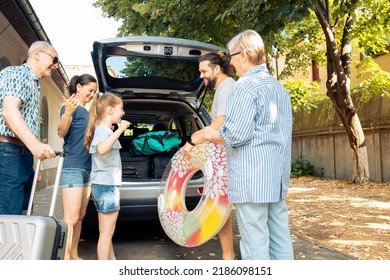 Happy people travelling at seaside with vehicle, leaving on vacation trip with parents, grandparents and small girl. Loading luggage and suitcase in automobile trunk, summer adventure. - Powered by Shutterstock