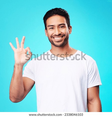 Happy, perfect gesture and portrait of a man in a studio with an agreement sign or expression. Happiness, smile and young Indian male model with an approval hand emoji isolated by a blue background.