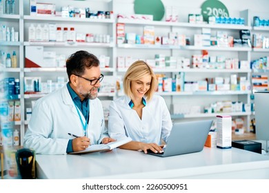 Happy pharmacist using laptop while her colleagues is taking notes in a pharmacy. - Powered by Shutterstock