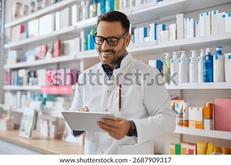 Happy pharmacist using touchpad while working in drugstore.