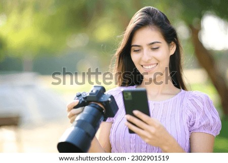 Happy photographer using phone and mirrorless camera in a park