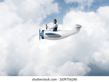 Happy pilot driving small propeller plane on background of blue sky with clouds. Traveling around the world by airplane. Funny man flying in small airplane. Cloudscape background with fluffy clouds.