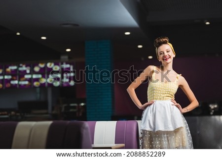 happy pin up waitress standing with hands on hips in cafe