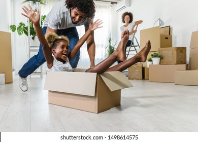 Happy Playful  African American Family Moving In New Apartment, Little Preschooler Daughter Sitting In Cardboard Boxes, Father Rolling Her,  Purchase Property Concept