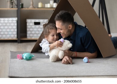 Happy Playful Daughter Kid And Loving Daddy Playing Tea Party In Toy Handmade House, Relaxing On Warm Floor Under Cardboard Paper Roof, Using Childish Colorful Plastic Dish. Childhood, Housing