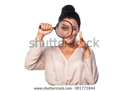 Happy playful female looking through a magnifying glass, giving a wink and pointing her finger at camera, over white background