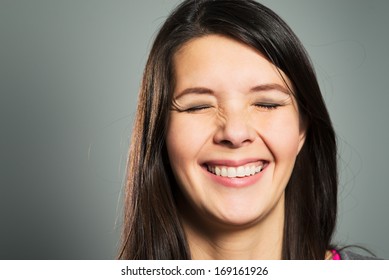 Happy pleased woman with a beaming toothy smile with her eyes closed, close up facial portrait on a grey studio background