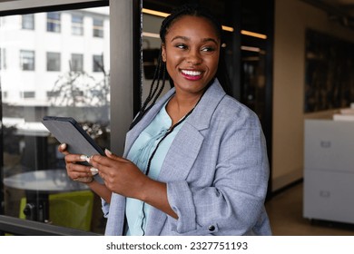 Happy plus size african american casual businesswoman using tablet in office window. Casual office, business, professional, communication and work, unaltered. - Powered by Shutterstock