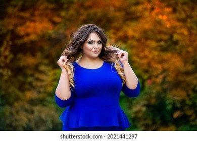 Happy plus size model in blue dress outdoors, fat woman in autumn park among yellow leaves, beauty in nature