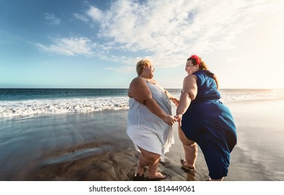 Happy plus size women dancing on the beach - Curvy overweight girls having fun during vacation in tropical destination - Over size confident people lifestyle concept 
