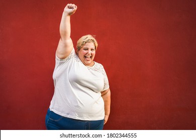 Happy plus-size woman celebrating and dancing for female power - Curvy overweight lady having fun with red background - Emancipation and confident concept - Focus on face