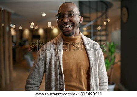 Happy portrait of african entrepreneur laughing and smiling. feeling excited and positive. Wearing trendy clothing and eye glasses in a modern working space