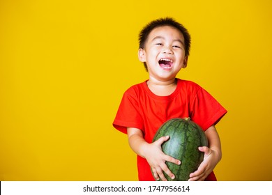 Happy Portrait Asian Child Or Kid Cute Little Boy Attractive Smile Wearing Red T-shirt Playing Holds Full Watermelon That Has Not Been Cut, Studio Shot Isolated On Yellow Background