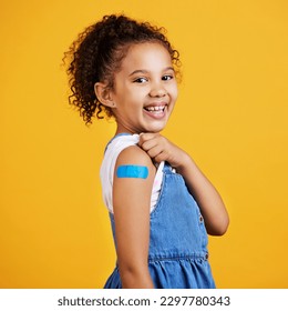 Happy, portrait and child with a plaster in a studio for a wound, sore or injury on her arm. Happiness, smile and healthy girl kid model posing with a bandaid after a vaccination by yellow background