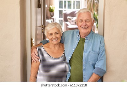 Happy portrait of a content senior man with his arm around his wife's shoulder while standing together at the front door of their home - Powered by Shutterstock